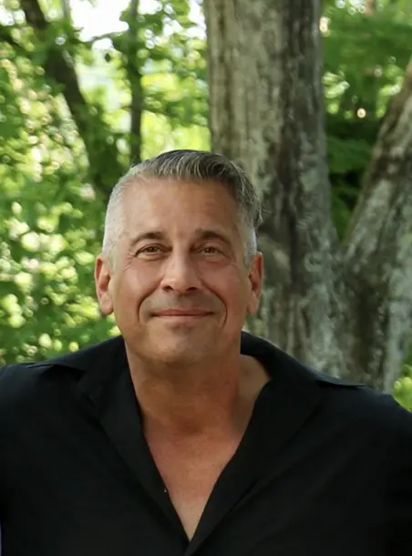 A man with grey hair sitting in front of a tree.